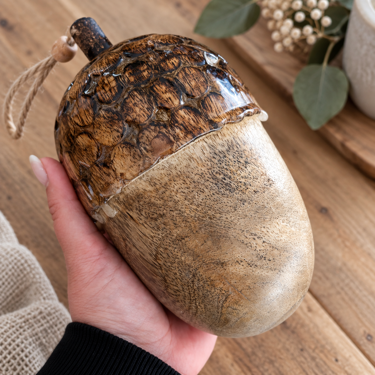 Große Deko-Eichel aus Holz mit strukturierter dunkelbrauner Kappe und natürlicher Holzmaserung, in einer Hand gehalten.