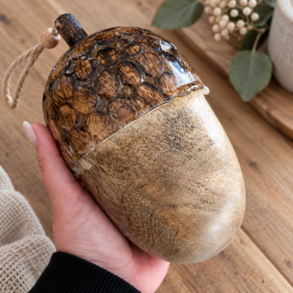 Große Deko-Eichel aus Holz mit strukturierter dunkelbrauner Kappe und natürlicher Holzmaserung, in einer Hand gehalten.