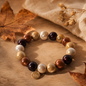 Perlenarmband mit 10 mm großen Perlen in warmen Herbstfarben, arrangiert auf einem natürlichen Hintergrund mit Herbstblättern und goldenem BIBA-Anhänger
