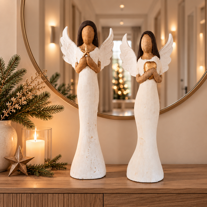 Zwei elegante Weihnachtsengel aus Holz in Weiß und Gold stehen auf einer Holzkommode in einem warm beleuchteten Flur mit weihnachtlicher Dekoration.