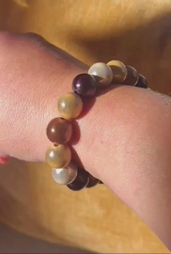 Braunes und mehrfarbiges Perlenarmband mit schimmernden Perlen in warmen Braun-, Beige- und Naturtönen, am Handgelenk getragen und in der Hand präsentiert.