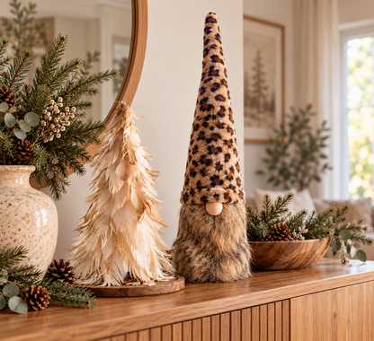 Stimmungsvolle Weihnachtsdeko auf einem Holzsideboard mit cremefarbenem Federbaum, großem Kuschelwichtel mit langer Leo-Mütze und natürlichem Tannengrün im gemütlichen Hygge-Stil.